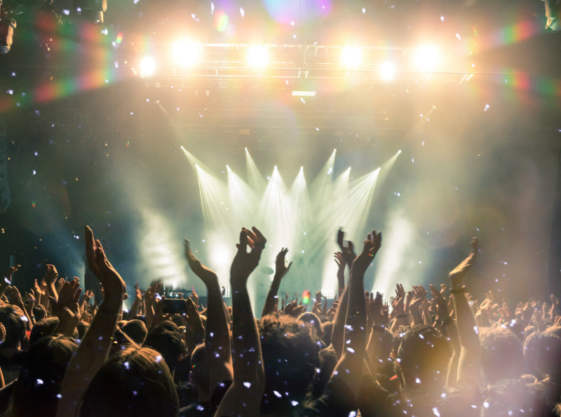 Creative Rest image. Image is of a crowd of people with their arms in the air enjoying a live music performance. 