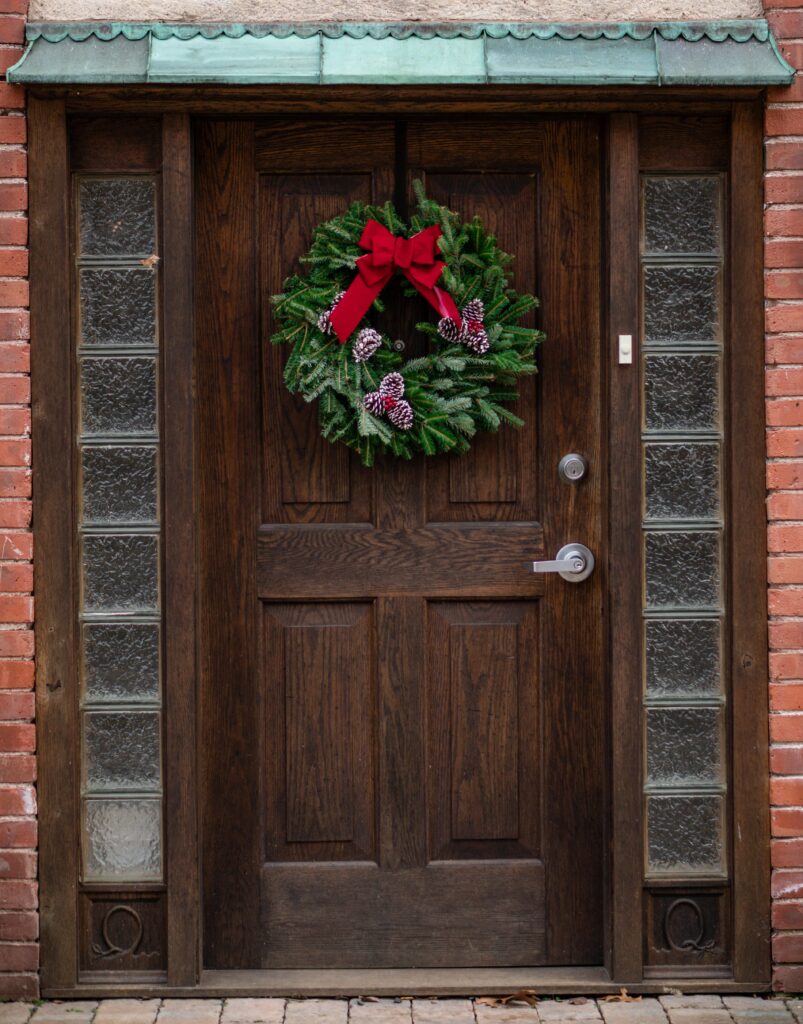 Image for Navigating the Holidays with Chronic Illness. Depicts a wooden door with a wreath with a red bow on it